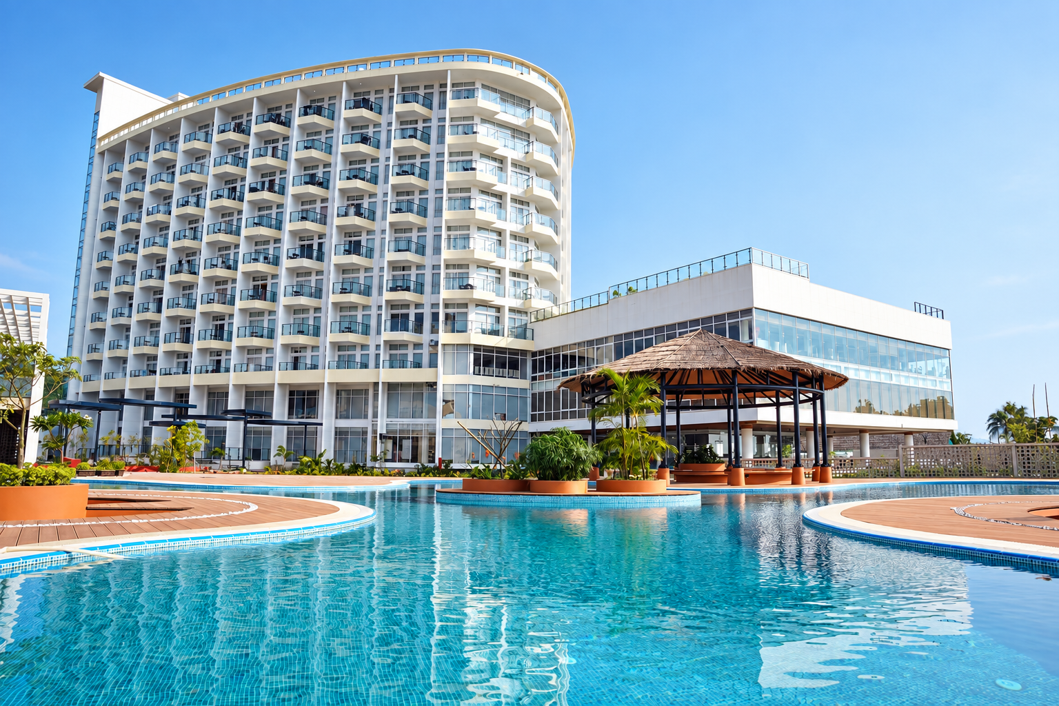 Curved white resort tower with a thatched pool bar beside a wide lagoon pool
